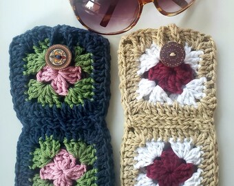 Pode incluir: Um par de óculos de sol castanhos repousa sobre duas capas de óculos de crochê. Uma capa é azul marinho com um design floral rosa e verde, e a outra é bege com um design floral bordô e branco. Cada capa tem um botão decorativo.