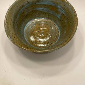 Puede incluir: Un cuenco de cerámica hecho a mano con un exterior moteado y terroso. El cuenco presenta una mezcla de tonos marrones, beiges y verde azulado, creando una estética rústica y única. El interior tiene un acabado brillante.