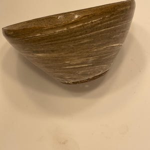 May include: A handmade ceramic bowl with a unique, asymmetrical shape. The bowl features a brown and white marbled design, with a glossy finish. The interior is a darker brown, and the exterior has a textured feel. This decorative bowl is perfect for serving or display.