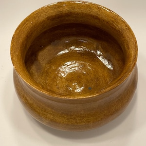 May include: A handcrafted, glazed ceramic bowl with a warm, earthy brown color. The bowl has a rounded shape with a slightly flared rim. The interior has a glossy finish, while the exterior has a textured appearance. This pottery bowl is suitable for serving or display.