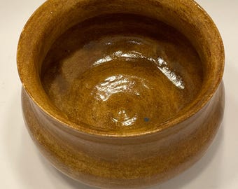 Puede incluir: Un cuenco de cerámica vidriada, hecho a mano, de color marrón cálido y terroso. El cuenco tiene una forma redondeada con un borde ligeramente ensanchado. El interior tiene un acabado brillante, mientras que el exterior tiene un aspecto texturizado. Ideal para servir o exhibir.