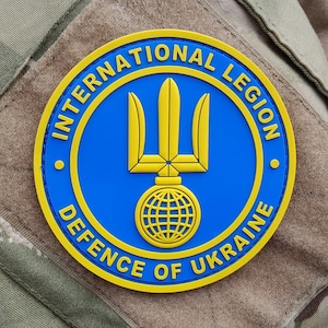 Może przedstawiać: Okrągła naszywka w kolorze żółtym i niebieskim z napisem "International Legion Defence of Ukraine" i symbolem trójzębu z globem u podstawy.