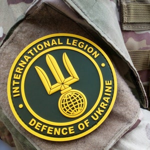 May include: A yellow and green circular patch with the text "International Legion Defence of Ukraine" and a trident symbol with a globe at the base.