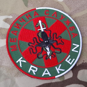 Könnte beinhalten: Ein gestickter Patch in Grün und Rot mit weißem Rand. Der Patch zeigt ein rotes Kreuz mit einem schwarzen Kraken und einem silbernen Schwert. Der Text "МЕДИЧНА СЛУЖБА КРАКЕН" ist in Weiß um den Rand des Patches geschrieben.