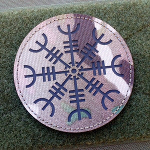 May include: A round, camouflage-patterned patch with a black, eight-pointed star design. The patch has a stitched edge.