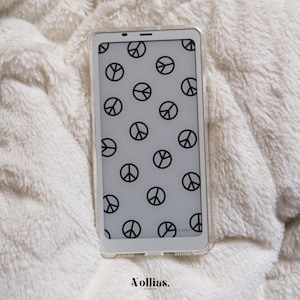Könnte beinhalten: Eine weiße Handyhülle mit durchsichtiger Rückseite und einem schwarzen Peace-Zeichen-Muster. Die Hülle liegt auf einer weißen, flauschigen Oberfläche.