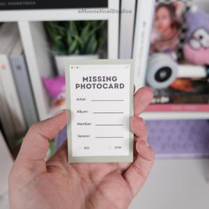 Pode incluir: Um cartão retangular verde-claro com um painel central branco apresentando o texto MISSING PHOTOCARD em letras negrito cinza-escuras. Abaixo do título, há quatro linhas em branco rotuladas como Artist, Album, Member e Version, com caixas de seleção ISO e OTW.