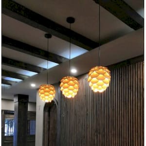 Puede incluir: Tres lámparas colgantes modernas con una pantalla de madera y papel en forma de piña. Las lámparas cuelgan de un techo negro en una habitación con paneles de madera.