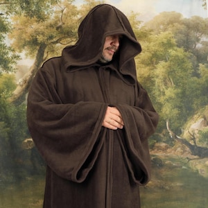 May include: A dark brown hooded robe featuring long, wide sleeves and a full-length design. The garment is constructed from a solid-colored, soft-textured fabric and includes a deep, structured hood that drapes over the head and shoulders.