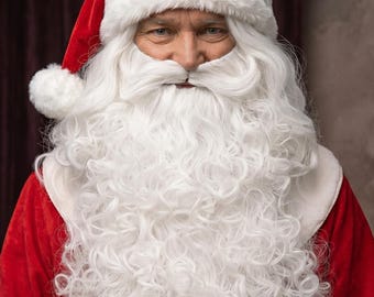 May include: A close-up of Santa Claus, dressed in a red velvet suit and hat with white fur trim. He has a long, curly white beard and mustache. The background is a dark, muted colour.