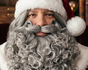 May include: A Santa Claus costume set featuring a deep red velvet hat with a thick white faux fur trim and a matching white pom-pom. The set includes a long, curly, silver-gray synthetic wig and a matching full beard with a curled mustache.