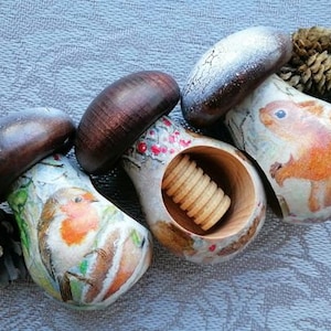 May include: Four wooden nutcrackers shaped like mushrooms with painted details. Each nutcracker features a different woodland creature: a robin, a squirrel, a deer, and a bear. The nutcracker with the robin has a red breast and is holding a nut in its beak. The nutcracker with the squirrel has a bushy tail and is holding a nut in its paws. The nutcracker with the deer has antlers and is standing on a log. The nutcracker with the bear has a brown coat and is holding a nut in its paws.