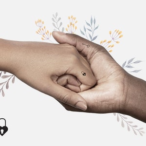 Puede incluir: Dos manos que se sostienen, con un pequeño tatuaje de un candado y una llave en los dedos. Las manos están rodeadas de flores de acuarela en tonos azules, amarillos y morados.
