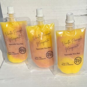 May include: Three pouches of yellow and peach-colored wax melts. The pouches are labeled "Vanilla Pineapple Margarita" and "Squeezable Wax Melt". The pouches are made in Alabama and are 3.5 oz (99g).