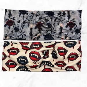 May include: Two headbands with a twisted knot design. One features a gray background with black roses, spiderwebs, and candles. The other has a cream background with red and black vampire lips.