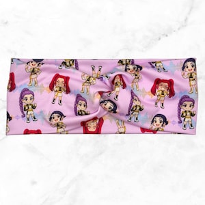 May include: A pink headband featuring a repeating pattern of cartoon figures with various hairstyles and outfits. The figures are in different poses, and the background has a sound wave design. The headband is twisted at the center.