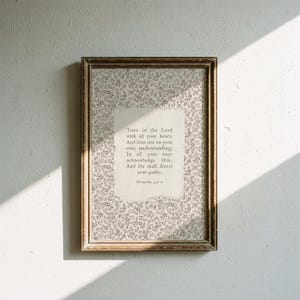 May include: A rectangular framed wall art piece featuring a light gray floral pattern background with a central off-white paper insert. The text reads: Trust in the Lord with all your heart, And lean not on your own understanding; In all your ways acknowledge Him, And He shall direct your paths. Proverbs 3:5-6.