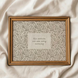 May include: A rectangular framed print with a floral patterned background and the text "His mercies are new every morning." The frame is a warm brown color, and the print is displayed on a white surface.