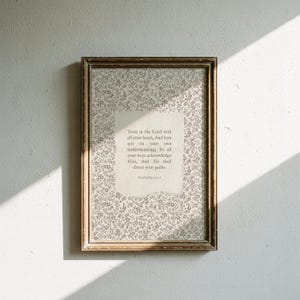 May include: A framed print with a floral patterned background and a central text block. The text reads "Trust in the Lord with all your heart..." The frame is a warm brown color, and the print is displayed against a white wall.