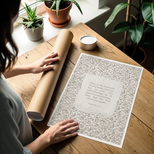May include: A print with floral patterns and text from Proverbs 3:5-6, displayed on a wooden table. A rolled-up poster and a small container are also on the table. The print's text reads: "Trust in the Lord with all your heart..."