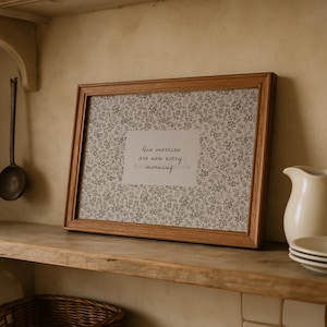May include: A framed print with a light brown wooden frame. The print features a floral pattern in shades of gray and white, with the text "His mercies are new every morning."