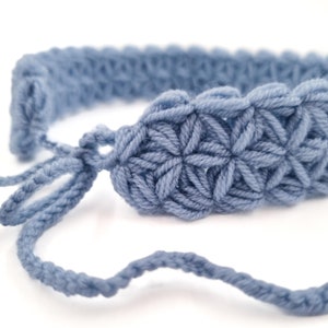May include: A light blue crocheted headband with a star-shaped stitch pattern. The headband is tied with a long, thin piece of yarn.