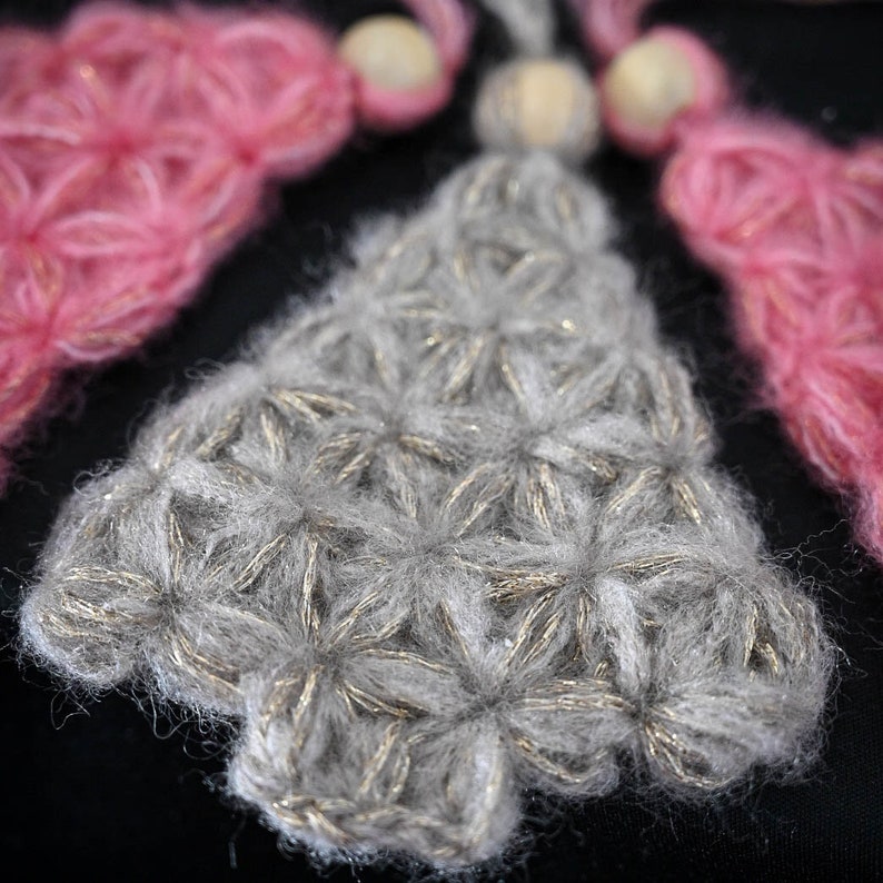 Gre and pink crocheted Christmas tree ornaments lying a on black table. The listing is for the pattern to crochet these trees with the jasmine stitch