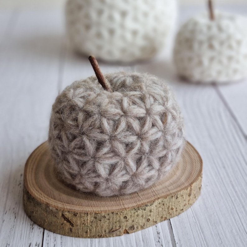 textured pumpkin sitting on a slab of wood. The pumpkin is beige and crocheted with the Jasmine Stitch. In the back we see one large and one small (2 sizes) pumpkins. The listing is for the pattern you need to make this modern fall decor