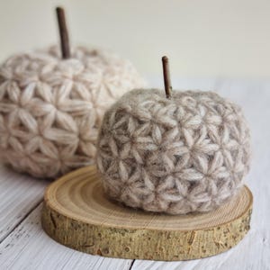 a textured pumpkin sitting on a slab of wood. The pumpkin is beige and crocheted with the Jasmine Stitch. In the back we see a larger, lighter colored pumpkin. The listing is for the pattern you need to make this modern fall decor