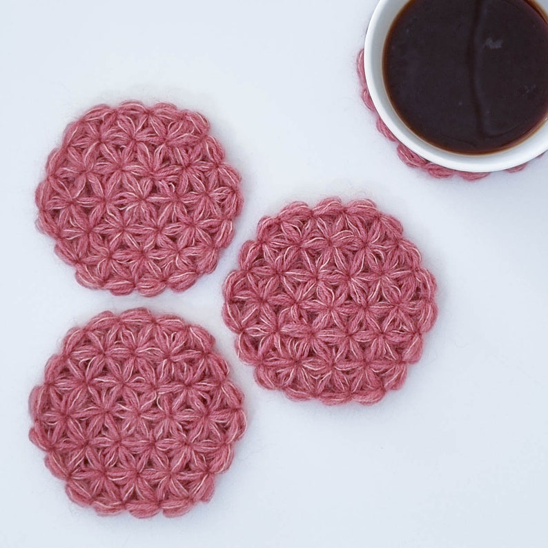 Puede incluir: Tres posavasos de ganchillo rosa con un patr&oacute;n de flores.