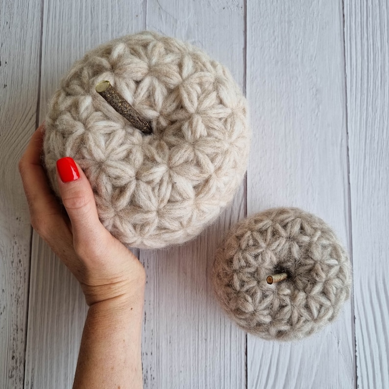 May include: Two beige crocheted pumpkins with a starburst pattern. The larger pumpkin has a twig attached to it.