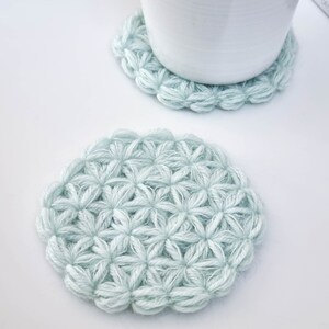 Puede incluir: Dos posavasos de ganchillo de color azul claro con un patr&oacute;n de flores. Los posavasos son redondos y tienen una textura en relieve.