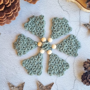 Green, small crocheted Christmas trees lying a on table. They are arranged in a circle. The listing is for the pattern to crochet these trees with the jasmine stitch