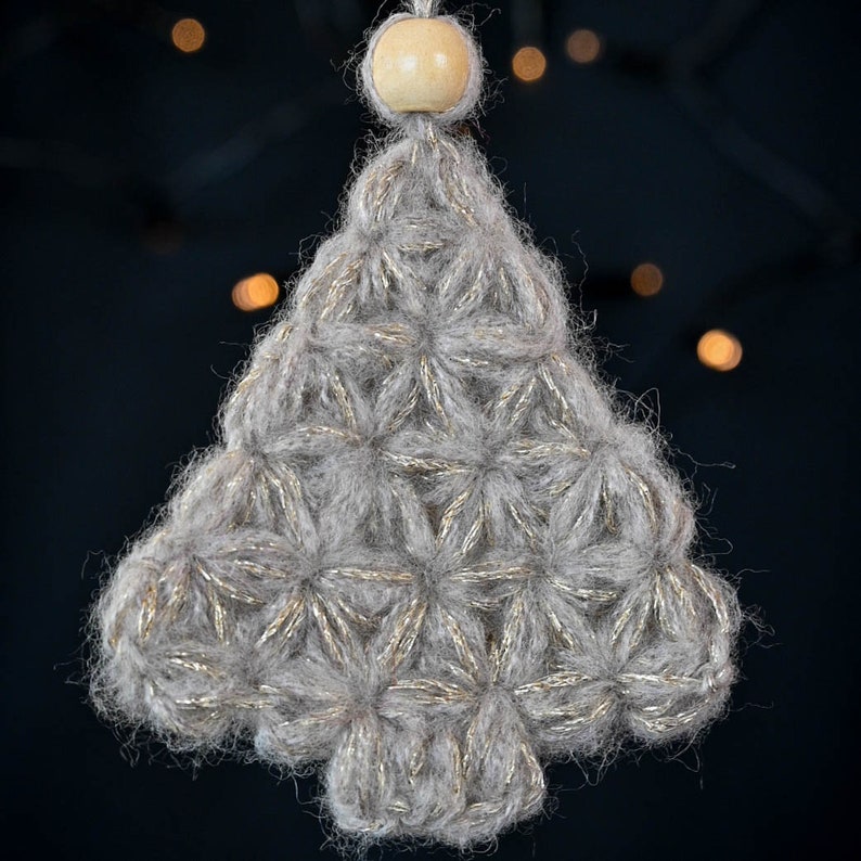 Puede incluir: Un adorno de &aacute;rbol de Navidad de ganchillo gris y dorado con una cuenta de madera en la parte superior.