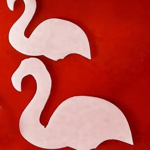 May include: Two white flamingo cutouts on a red background. The flamingo shapes are smooth and have a curved neck and body. The cutouts are likely for crafting or decorative purposes.