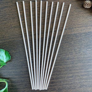 Peut inclure: Dix bâtonnets diffuseurs en bois de couleur naturelle disposés en éventail sur une surface en bois brun.