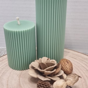 May include: Two green pillar candles with a ribbed texture on a wooden surface with decorative accents.
