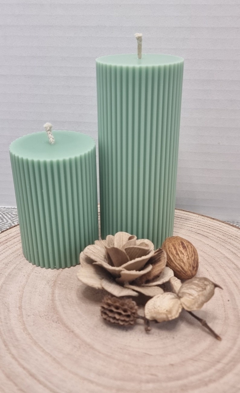 May include: Two green pillar candles with a ribbed texture on a wooden surface with decorative accents.