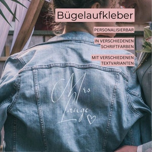 Könnte beinhalten: Eine blaue Jeansjacke mit einem weißen Bügelbild, auf dem "Mrs. Lange" mit einem Herz steht. Der Text "Bügelaufkleber" befindet sich oben im Bild, und der Text "PERSONALISIERBAR", "IN VERSCHIEDENEN SCHRIFTFARBEN" und "MIT VERSCHIEDENEN TEXTVARIANTEN" befindet sich unter dem Bild.