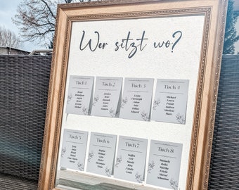 May include: A gold-framed mirror with the German text "Wer sitzt wo?" (Who sits where?) and eight table cards. Each card lists names and is decorated with a floral design, ideal for a wedding or event.