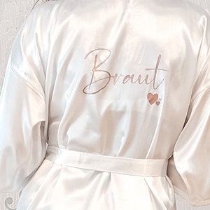 Könnte beinhalten: Weiße Satin-Robe mit dem Wort "Braut" in roségoldenen Lettern und zwei kleinen roségoldenen Herzen.