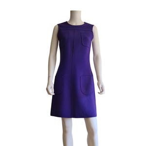Puede incluir: Vestido morado sin mangas, hasta la rodilla, con dos bolsillos delanteros y dos bolsillos en el pecho. El vestido se exhibe en un maniquí. El vestido tiene un diseño sencillo y clásico.
