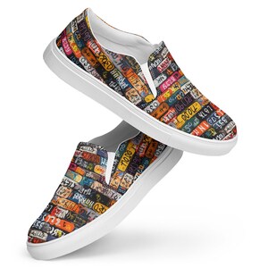 May include: A pair of white canvas slip-on shoes with a colorful pattern of license plates. The pattern includes numbers, letters, and words like "831", "039", "71000", "UNIPOST", and "LOTA 2".