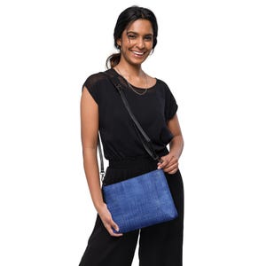 May include: A blue denim crossbody bag with a black adjustable strap. The bag has a rectangular shape and a textured fabric.