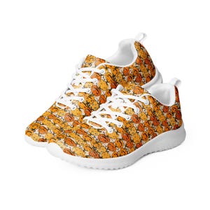 May include: White sneakers with a pattern of orange and yellow cartoon faces. The shoes have a white sole and laces.
