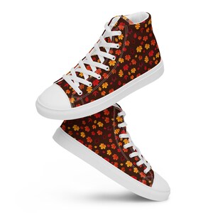 May include: White high-top sneakers with a brown canvas featuring a pattern of orange, red, and yellow autumn leaves.