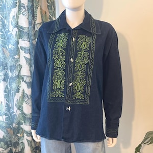 May include: A dark blue long-sleeve shirt featuring bright green embroidered floral and paisley patterns on the front panels and collar. The shirt includes a button-down front with light-colored buttons and long sleeves with matching green zigzag embroidery on the cuffs.