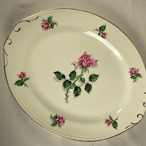 May include: Oval serving platter with a cream-colored background and a gold rim. The platter is decorated with pink roses and green leaves. The roses are in various stages of bloom, and the platter has a decorative edge.