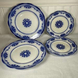 May include: Four antique white and blue porcelain plates. The plates have a scalloped edge with a blue floral design. The center of each plate features a blue floral pattern. The plates are arranged on a white surface.
