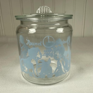 Puede incluir: Un tarro de cristal transparente con tapa, con un diseño azul claro de niños y las palabras "Round the clock" y "24 hours a day". El tarro tiene forma redonda y una tapa de cristal transparente.